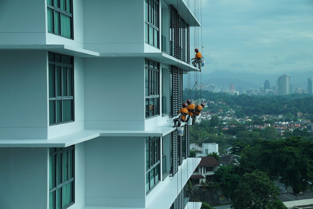 maintenance workers hang off the side of an apartment building