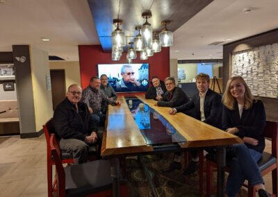 iTel Sales Team catching up over a drink in a hotel lobby, sitting around a live-edge wooden table with a tv in the background